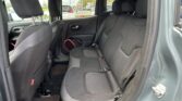 Interior of a car's rear passenger area with black cloth seats and headrests, door open, view of a parking lot outside the windows