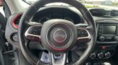 Steering wheel with Jeep logo and red stitching, dashboard gauges visible behind it, car interior in view.