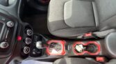 Interior of a car showing a red-accented center console with the gear shifter, climate controls, and red-stitched seats/armrest.