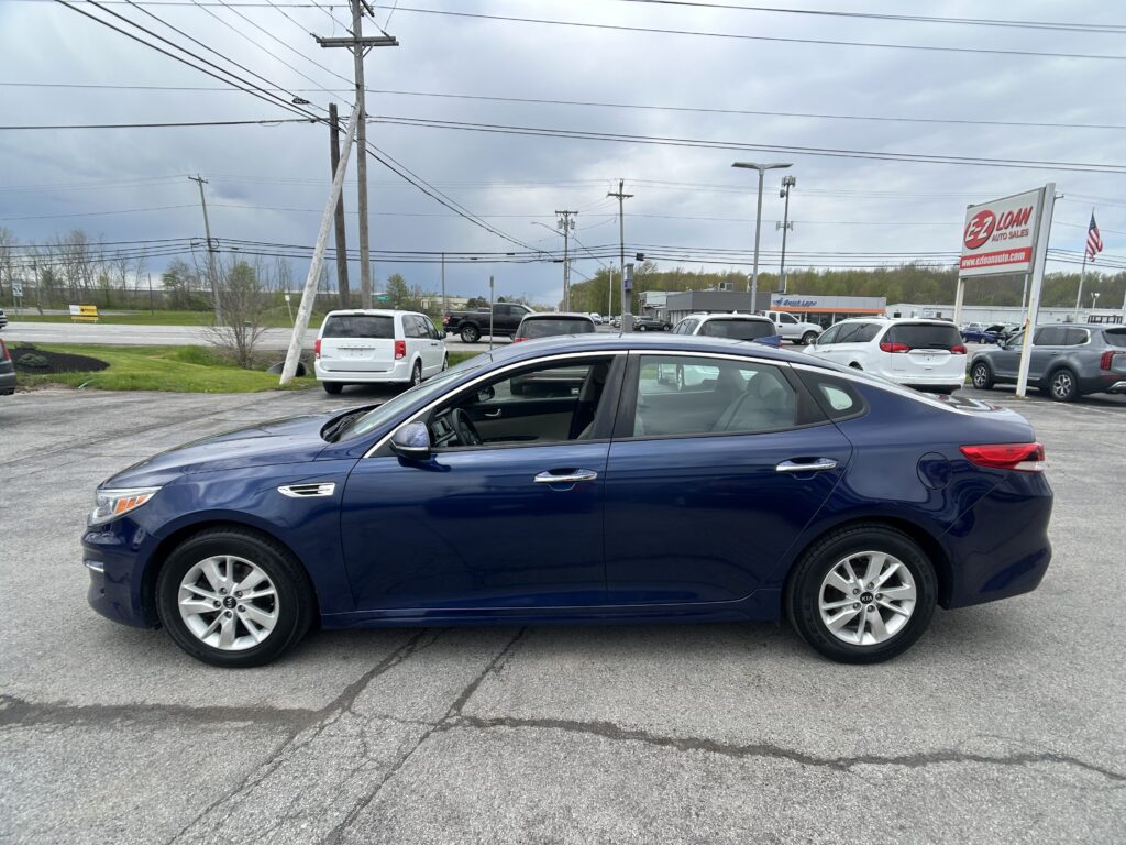 Blue sedan in a car dealership lot with other vehicles, utility poles, and an EZ Loan Auto Sales sign in the background.