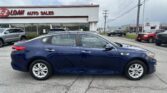 Blue sedan in a car lot with a dealership building in the background and power lines overhead.