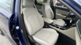 Open car door exposing light-gray front seats and center console in a blue vehicle interior, steering wheel visible on the right side of the image and keys in the ignition area.