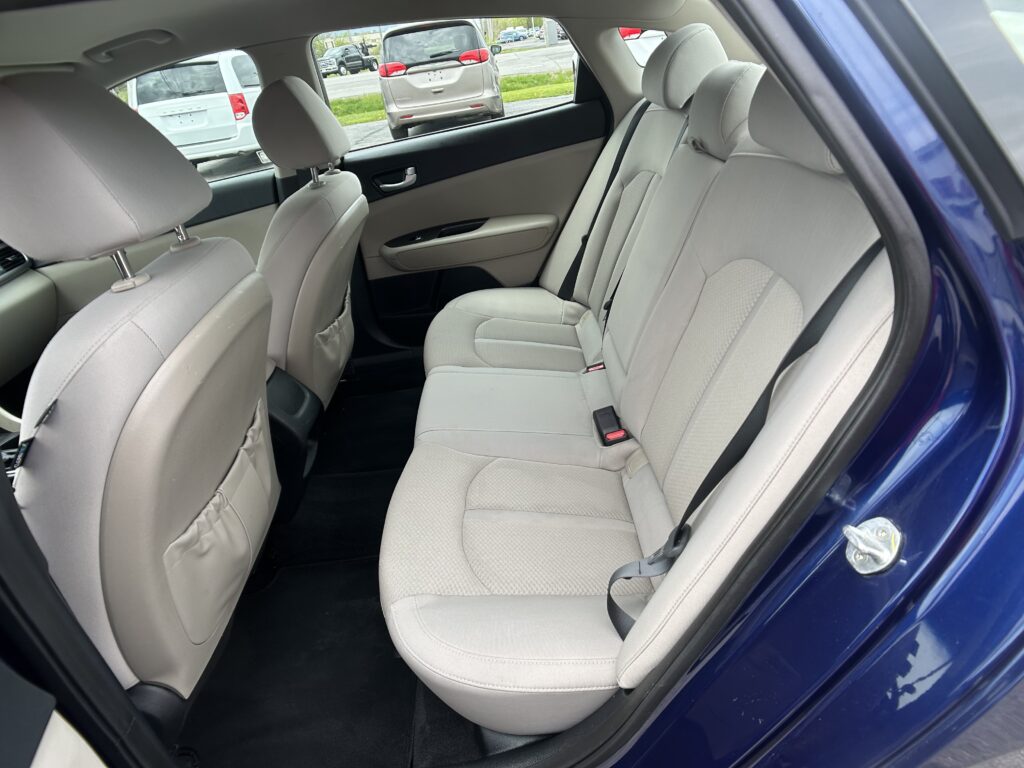 Rear interior of a blue sedan with beige fabric seats, a three-seat bench and headrests visible.