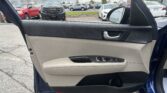 View of a car's open front passenger door from inside, showing the beige and black interior and parking lot outside with trucks and cars.