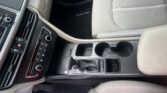 Beige car interior showing the center console with gear shifter, cup holders, and climate controls next to a light-colored passenger seat.