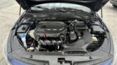 Front view of a car with the hood raised, exposing the engine bay and components like the battery and coolant reservoir. Kia badge visible on the grille.
