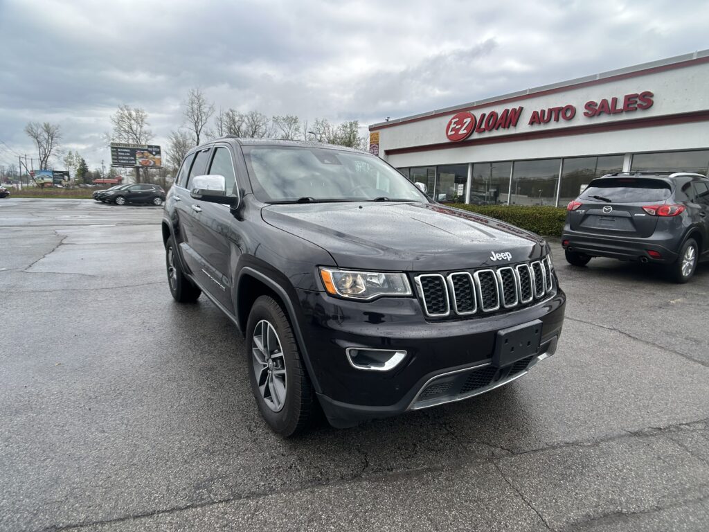 Black Jeep SUV in a parking lot in front of an EZ LOAN Auto Sales storefront on a cloudy day.
