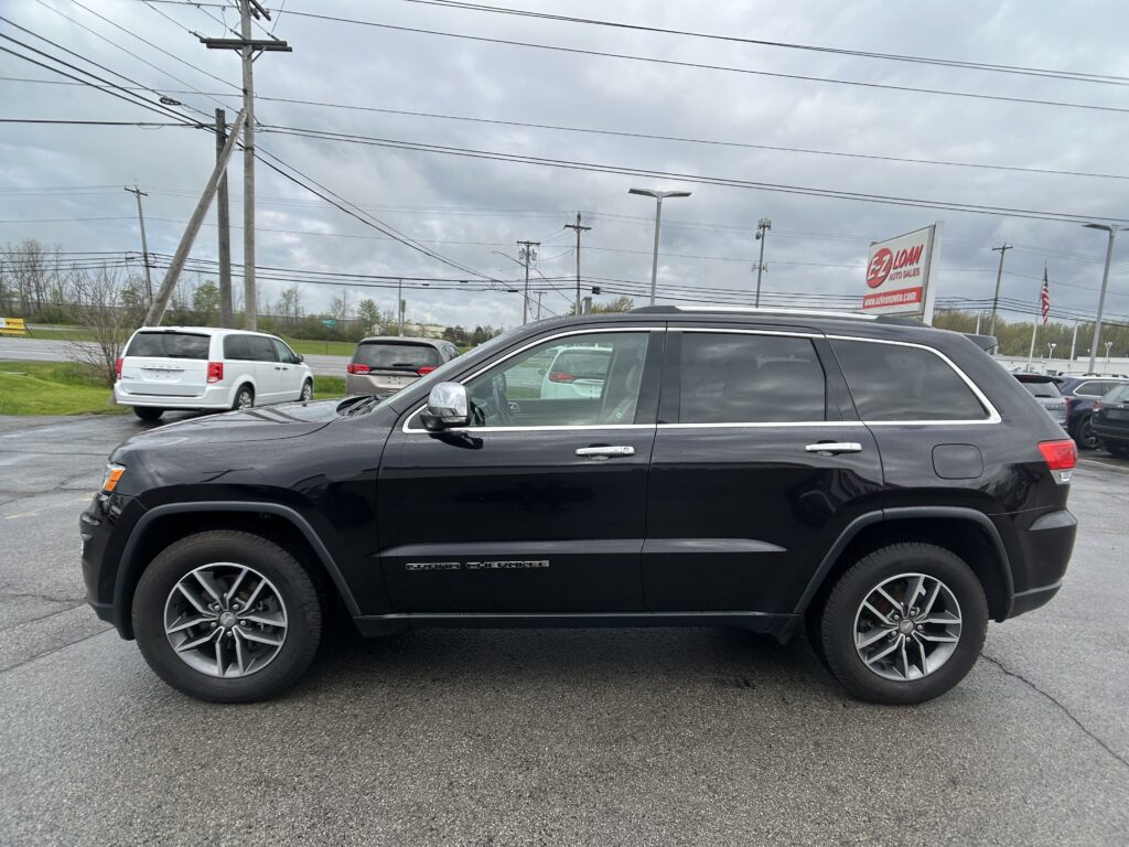 Black Jeep Grand Cherokee in a dealership lot with a red EZ Loan Auto Sales sign and utility poles in the background