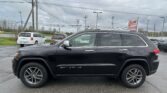 Black Jeep Grand Cherokee in a dealership lot with a red EZ Loan Auto Sales sign and utility poles in the background