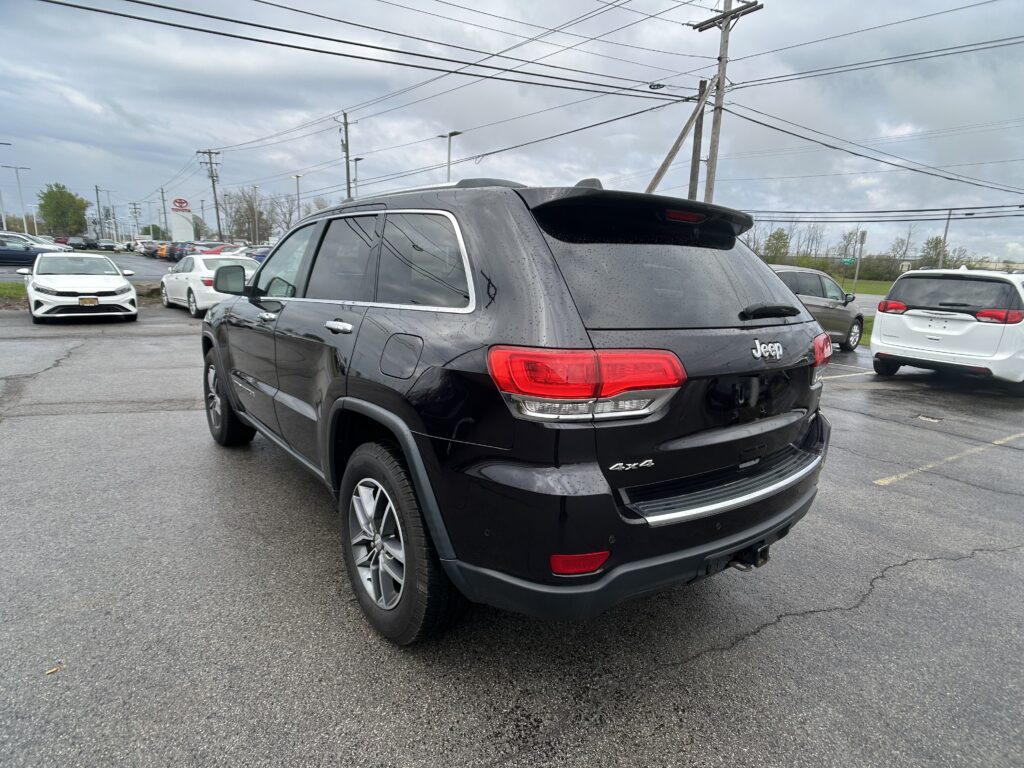 Rear three-quarter view of a black Jeep SUV parked in a wet lot with other cars and power lines overhead.