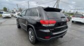 Rear three-quarter view of a black Jeep SUV parked in a wet lot with other cars and power lines overhead.