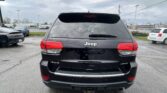 Rear view of a black Jeep SUV in a parking lot on a rainy day, raindrops on the rear window and taillights visible.