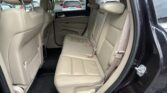 Beige leather back seat of a SUV with three seating positions and headrests, view from open rear door.