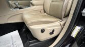 Interior of a beige leather car with the driver’s seat and center console; gear shifter and steering wheel visible, door panel and seatbelt nearby.