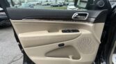 Interior of a car door: beige upholstery, wood trim, chrome door handle, controls for windows and mirrors visible.