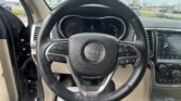 Inside a Jeep cockpit viewed from the driver’s seat, steering wheel and digital gauge cluster, with a parking lot outside the windshield.
