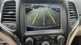 Infotainment screen showing a rearview camera view with parking guideline lines in green, yellow, and red over a parking lot; text reads 'Check Entire Surroundings'.