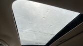Panoramic sunroof view from inside a car, with raindrops beading the glass and a gray, overcast sky outside.