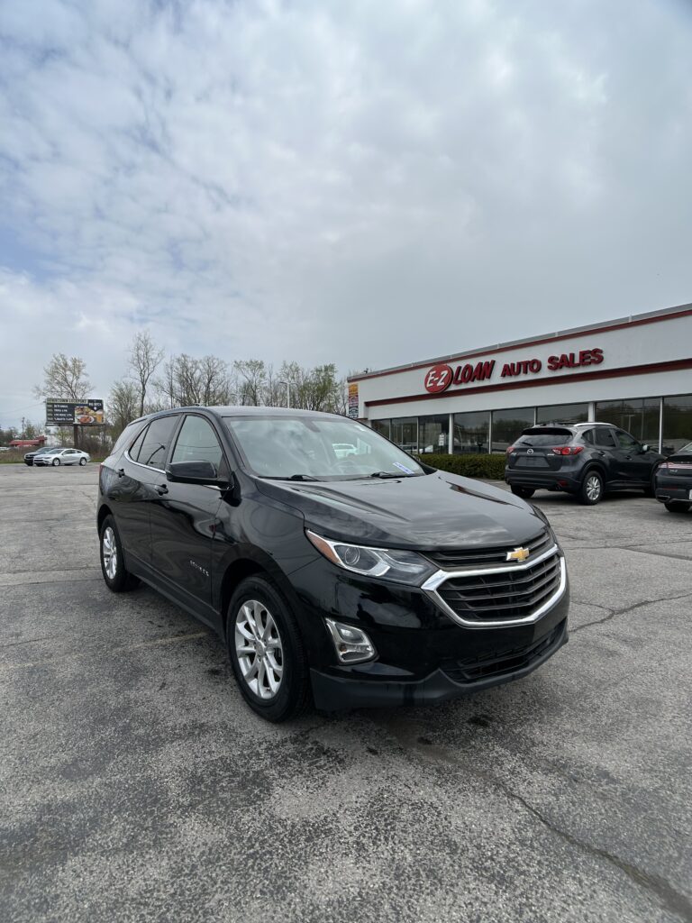 Black Chevrolet SUV in the foreground of a car lot, with an EZ LOAN AUTO SALES storefront in the background and cloudy sky above.