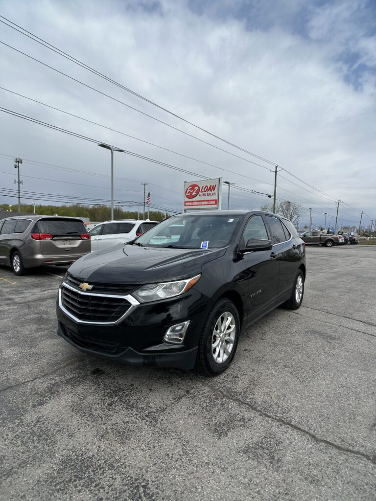 Black Chevrolet SUV in the foreground at EZ Loan Auto Sales lot with a sign and other cars behind.