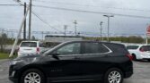 Black Chevrolet Equinox SUV in a parking lot, with utility poles and power lines overhead under a cloudy sky