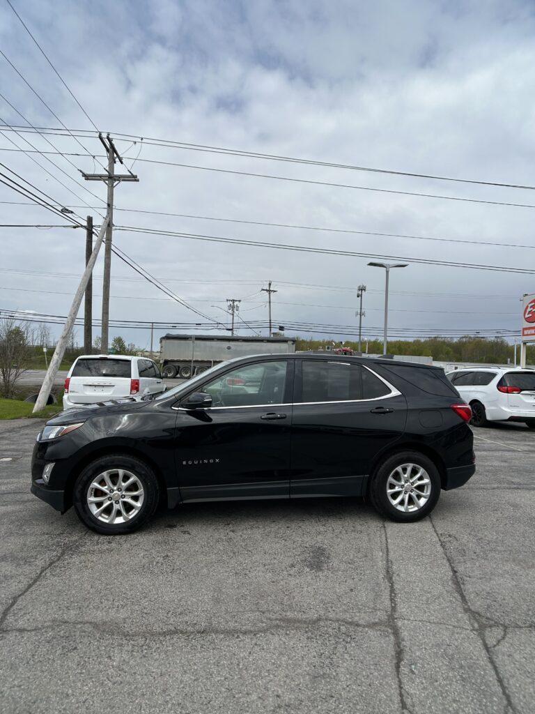 Black Chevrolet Equinox SUV in a parking lot, with utility poles and power lines overhead under a cloudy sky