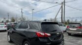 Black Chevrolet Equinox parked in a dealership lot with overhead power lines and several other cars nearby.