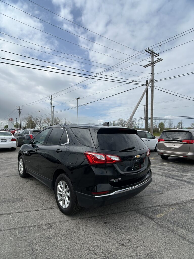 Black Chevrolet Equinox parked in a dealership lot with overhead power lines and several other cars nearby.