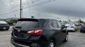 Black Chevrolet SUV (AWD LT) parked in a dealership lot, with power lines overhead and other cars in the background.