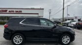 Black Chevrolet Equinox parked in a dealership lot with a building that reads ‘Auto Sales’ and a cloudy sky.