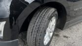 Close-up of a black SUV's front wheel and fender, showing the tire and glossy body with sky reflections.