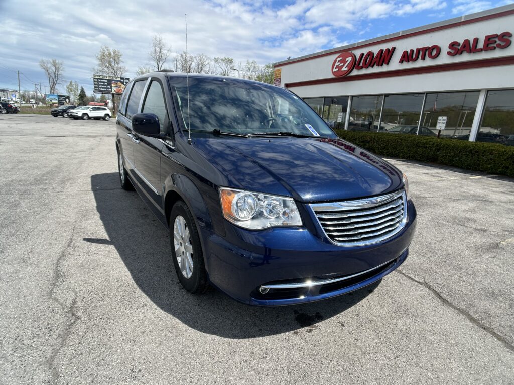 Dark blue minivan parked diagonally in a car lot in front of a dealership building with an EZ Auto Sales sign in red letters.