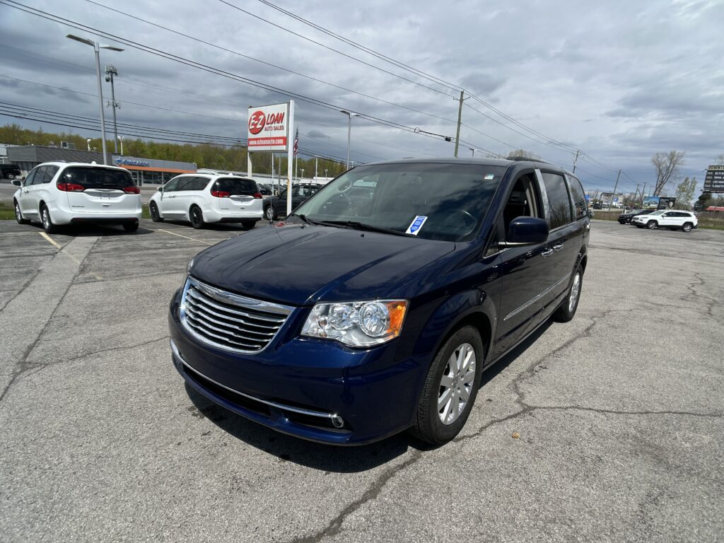 Blue SUV in the foreground at a car dealership lot with white vans and an EZ Auto Sales sign in the background on a cloudy day.