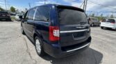 Rear three-quarter view of a dark blue Town & Country minivan parked in a busy car lot with other vehicles and power lines overhead.