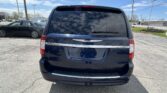 Rear view of a dark blue Chrysler Town & Country minivan parked in a lot, reflections of clouds visible on the rear window.