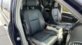 Interior of a dark leather SUV with front seats visible through an open front door, dealership lot seen outside the window.