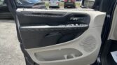 Interior of a car door showing the window/control panel, door handle, and speaker with a parking lot of cars beyond the open door