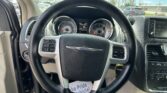 Driver's view of car interior: steering wheel, gauge cluster, and dashboard; parked cars seen through the windshield.