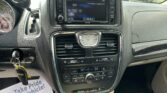 Center dashboard of a car showing an infotainment screen, climate controls, and a key in the ignition on the left; paper on the passenger side reads 'We Take Pride In Your Vehicle'.