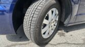 Close-up of a car tire mounted on a blue SUV, wheel and fender visible on asphalt.