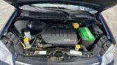 Under-hood view of a car engine bay with a glossy black engine cover labeled 3.6L VVT, yellow hood latch, and a bright green car battery on the right side.