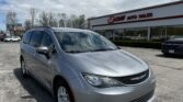 Silver minivan in the foreground outside an EZ Loans Auto Sales storefront on a sunny day with a blue sky and clouds.