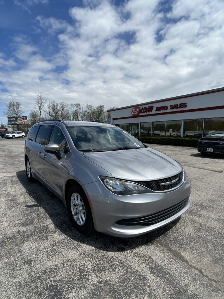 Silver minivan in the foreground outside an EZ Loans Auto Sales storefront on a sunny day with a blue sky and clouds.