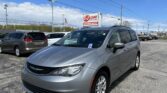 Silver minivan in the foreground at a car dealership lot, with an E-Z LOAN Auto Sales sign in the background and a blue sky above.