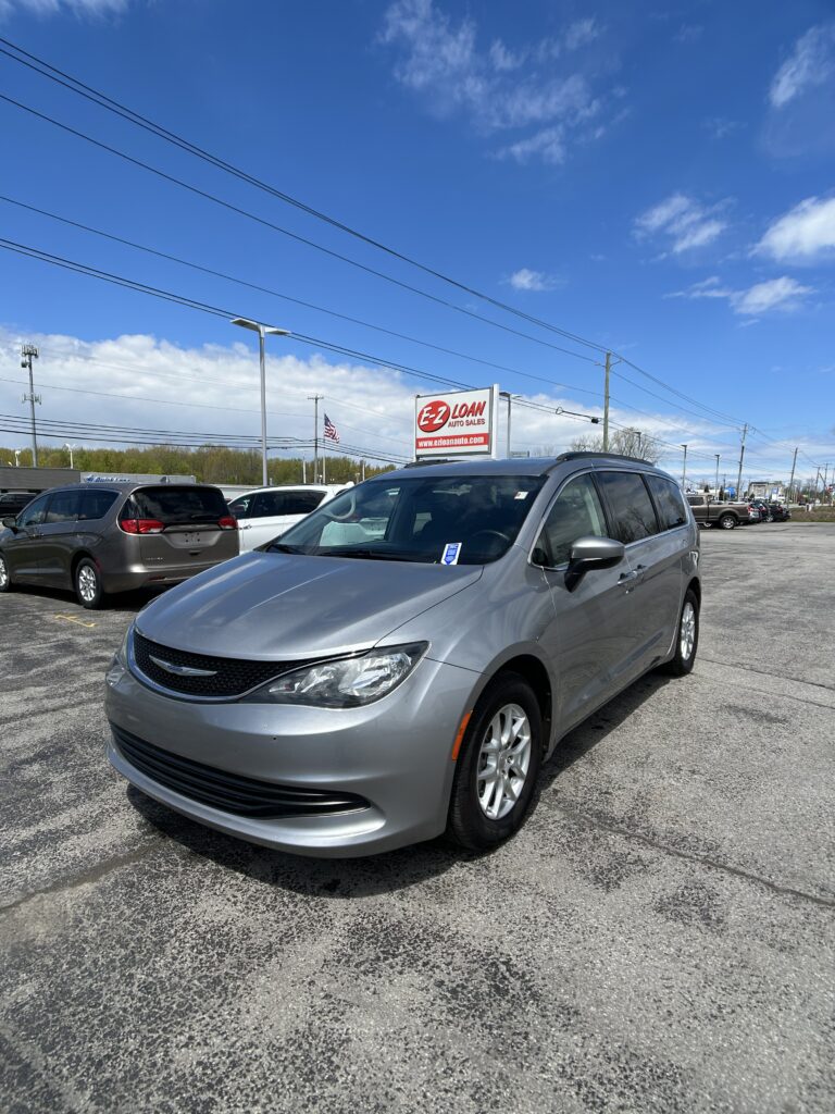 Silver minivan in the foreground at a car dealership lot, with an E-Z LOAN Auto Sales sign in the background and a blue sky above.
