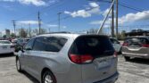 Rear three-quarter view of a silver Chrysler Voyager minivan in a parking lot, with tall power lines and a blue sky above.