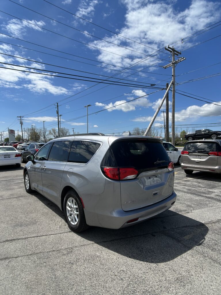 Rear three-quarter view of a silver Chrysler Voyager minivan in a parking lot, with tall power lines and a blue sky above.