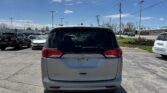 Rear view of a silver Chrysler Voyager minivan parked in a lot with other cars and a blue sky with power lines overhead.