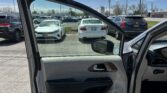 Driver's side car door is open, showing a gray interior in a crowded parking lot under a blue sky with scattered clouds.