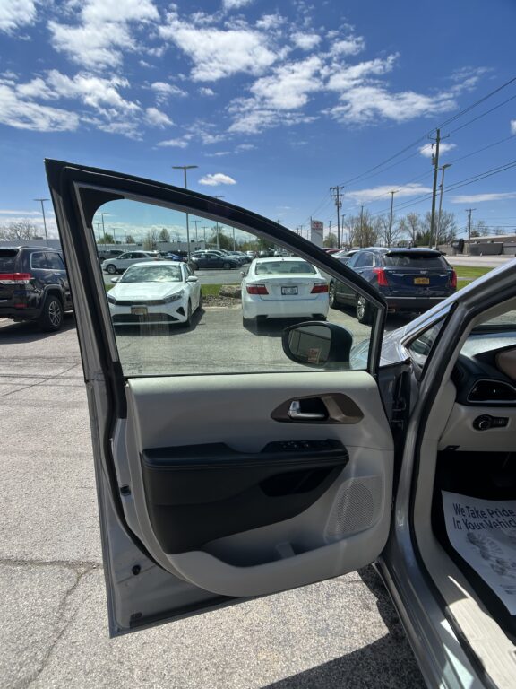 Driver's side car door is open, showing a gray interior in a crowded parking lot under a blue sky with scattered clouds.